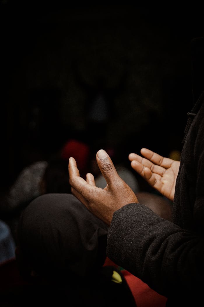 Hands raised in prayer during a solemn religious gathering indoors, evoking a sense of spirituality and devotion.