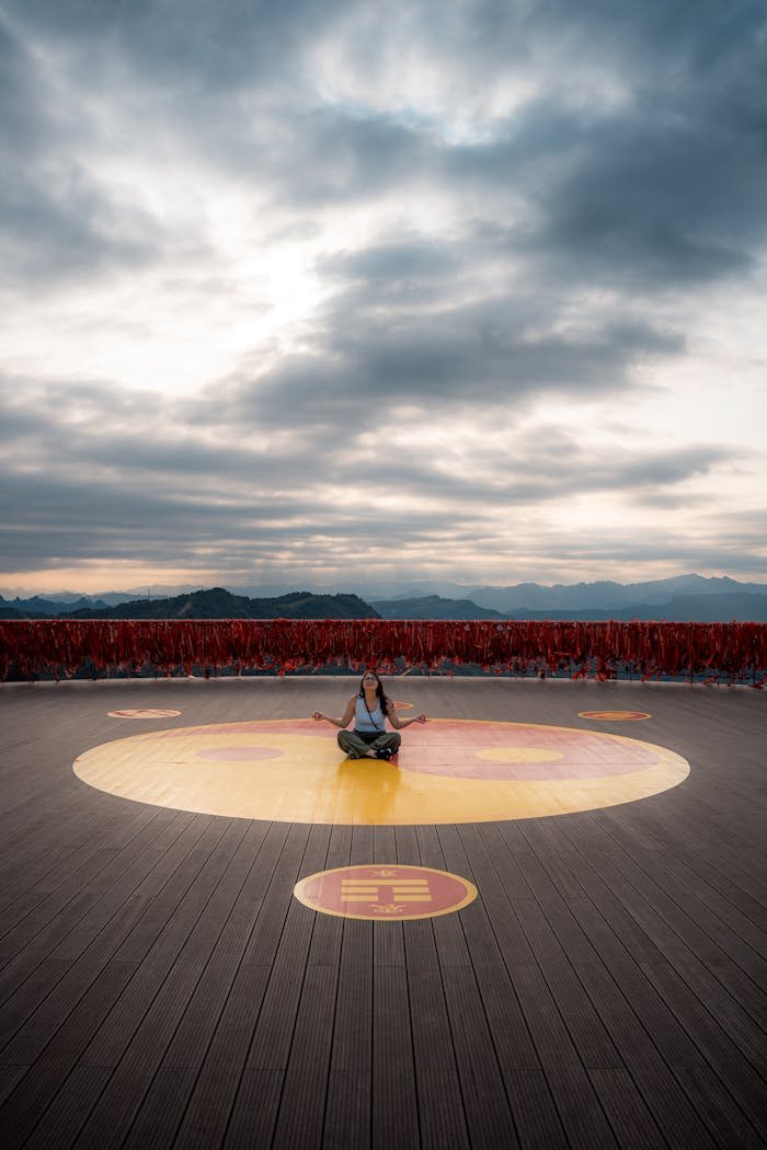 Person meditating on a platform in Guilin, China, with mountains under a dramatic sky.