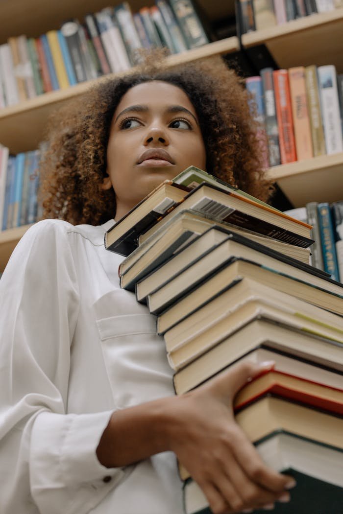 African American woman holding a stack of books in a library setting, emphasizing knowledge and learning.