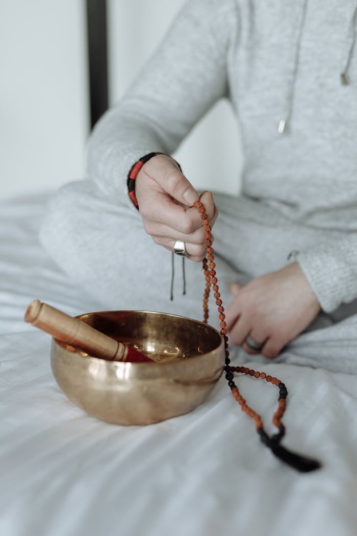 Person in meditation holding prayer beads with a Tibetan singing bowl in focus, conveying spiritual tranquility.