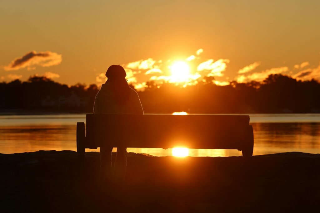 person alone on bench at sunset by the water